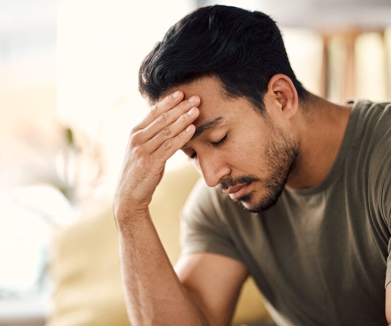 A man sitting with his hand on his forehead, appearing stressed or tired - Headache