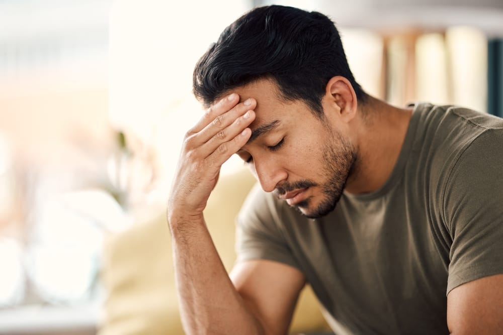 A man sitting with his hand on his forehead, appearing stressed or tired - Headache